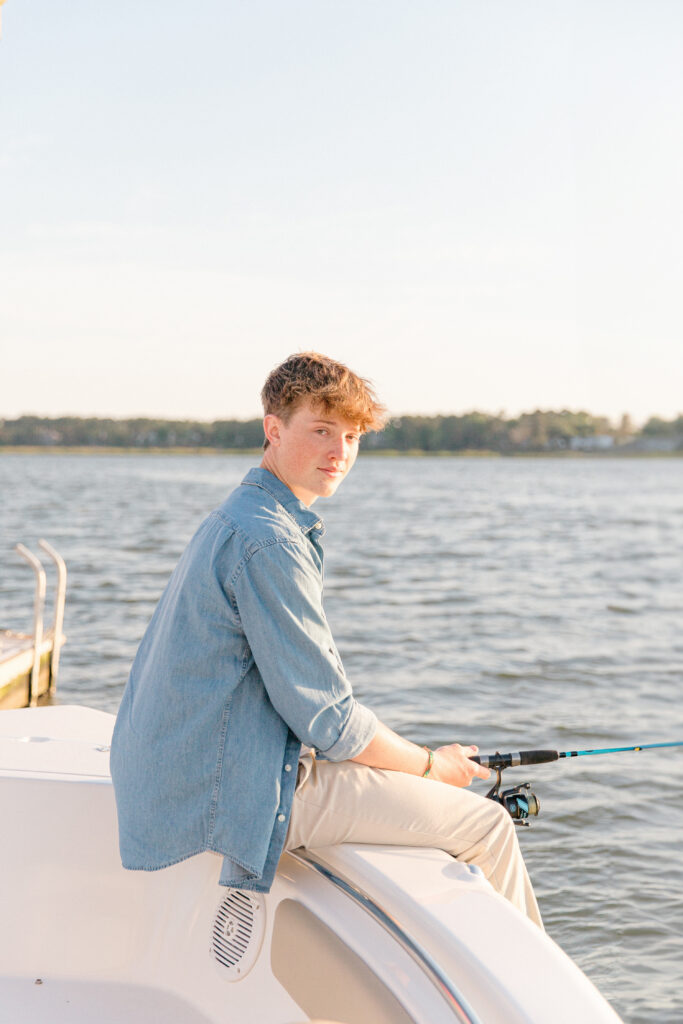 A young man sitting on his boat fishing on the May River at sunset for his senior portrait session with Bluffton Senior Photographer