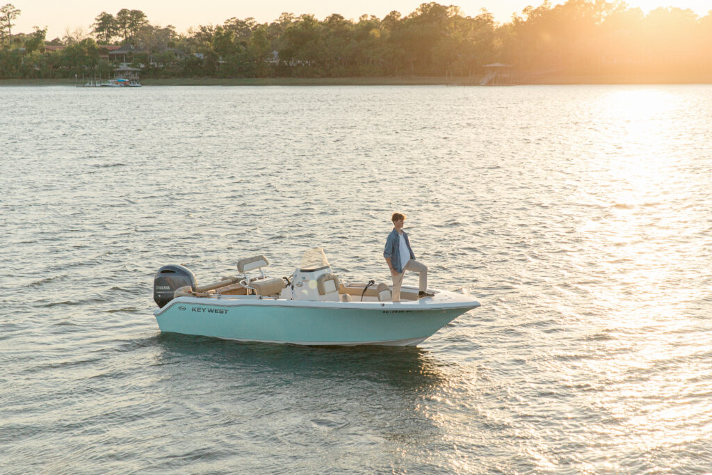 A young man standing in a captains pose on the bow of his boat on the May River in Bluffton, SC during sunset for his Senior Portrait Session